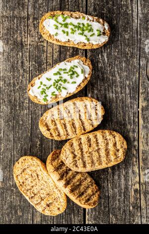 Pane croccante con formaggio cremoso e erba cipollina su tavolo di legno. Vista dall'alto. Foto Stock