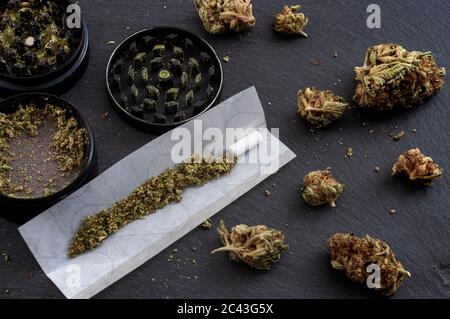 Preparare un tema di concetto di paraphernalia comune e di droga con la trave di erbe usata per macinare le gemme di cannabis e rotolare le articolazioni della marijuana, accanto alla carta rotabile A. Foto Stock