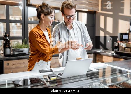 Due giovani manager o proprietari di negozi che hanno qualche discussione al banco del negozio o del bar. Concetto di gestione delle piccole imprese Foto Stock
