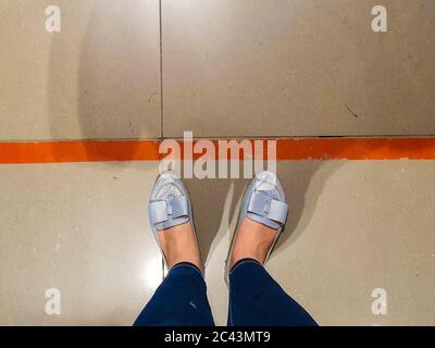 La persona si trova in linea rossa mantenendo la distanza sociale sicura a causa delle gambe pandemiche di ragazza in jeans che aspettano in fila al banco cassa nel supermercato Top Foto Stock