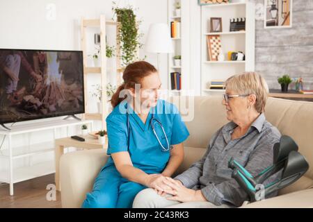 Assistente femminile che parla con la donna anziana in casa di cura con le stampelle. Foto Stock