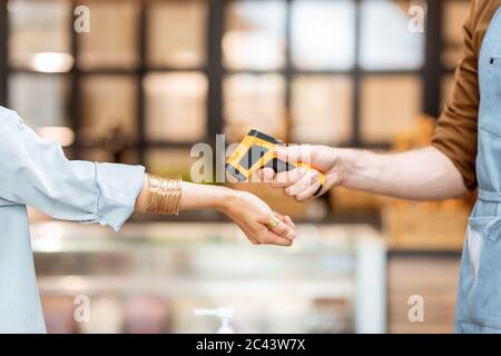 Controllo della temperatura dei visitatori di bar o negozi durante l'ingresso, primo piano. Concetto di nuove regole per il business durante la pandemia Foto Stock