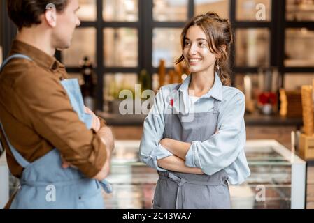 Ritratto di due allegri dipendenti di un bar o di un piccolo negozio di fronte al bancone all'interno Foto Stock