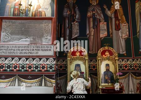 Snagov, Romania - 21 giugno 2020: La donna anziana che indossa una maschera Covid-19 prega fuori di una chiesa ortodossa cristiana. Foto Stock