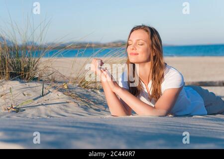 Ritratto di donna sorridente sdraiata sulla spiaggia godendo del sole, Sardegna, Italia Foto Stock