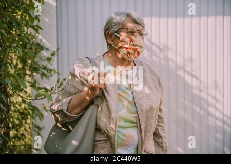 Donna anziana che indossa la maschera mentre cammina all'aperto durante l'epidemia pandemica Foto Stock