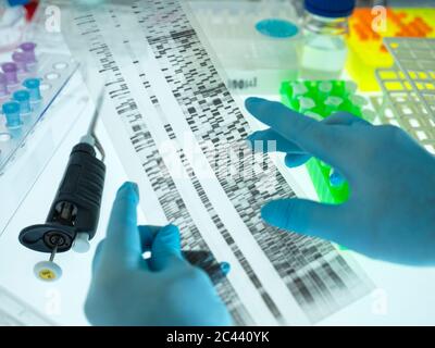 Mani di scienziati che indossano guanti chirurgici che analizzano il grafico dei risultati del sequenziamento del DNA Foto Stock