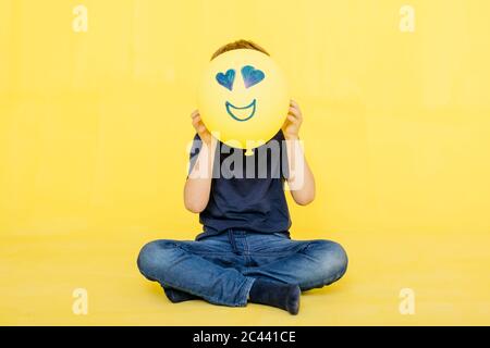 Ragazzo che tiene il pallone giallo con faccia antropomorfa su sfondo colorato Foto Stock