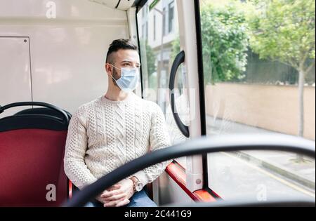 Ritratto di giovane uomo che indossa una maschera protettiva seduto in autobus pubblico che guarda fuori dalla finestra, Spagna Foto Stock