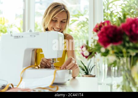 Donna sorridente cucire maschere a casa Foto Stock