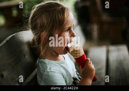 Ragazza che mangia gelato seduto su panca Foto Stock