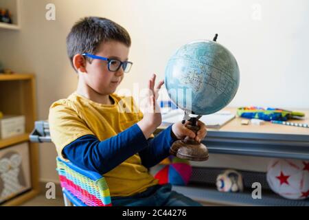 Simpatico ragazzo che tiene mentre tocca il globo a casa durante la pandemia COVID-19 Foto Stock