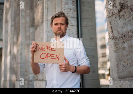 Negoziante in possesso di cartone con annuncio di apertura in città Foto Stock