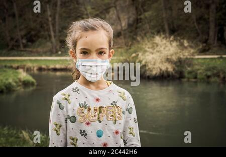 Ritratto di ragazza triste in piedi con maschera autosegn viso a riva del fiume in foresta Foto Stock