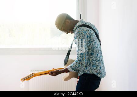 Sorridente giovane musicista pop che suona la chitarra per finestra Foto Stock