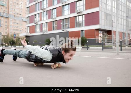 Ragazza spensierata sdraiata mentre skateboard su strada contro la costruzione Foto Stock