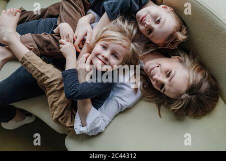 Vista ad alto angolo della madre felice che giace con i figli sul divano nel soggiorno di casa Foto Stock