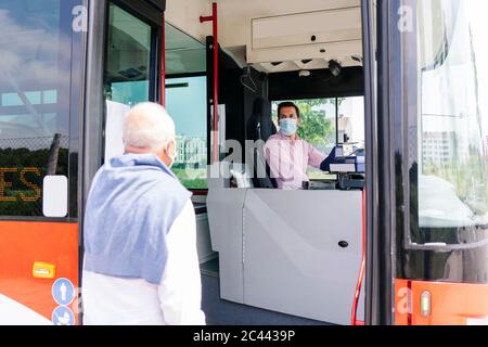 Autista dell'autobus che indossa una maschera protettiva che parla con il passeggero alla fermata dell'autobus, Spagna Foto Stock