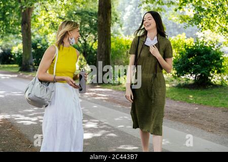 Due donne felici che si incontrano nella natura mentre indossano maschere di faccia lasciate giù Foto Stock