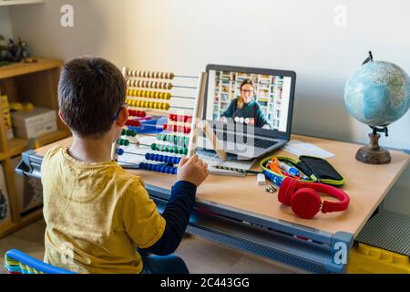 Ragazzo che usa abacus con insegnante in videochiamata durante la casa Foto Stock