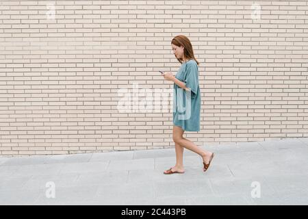 Donna che usa lo smartphone mentre cammina per strada Foto Stock