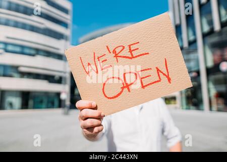 Negoziante in possesso di cartone con annuncio di apertura in città Foto Stock