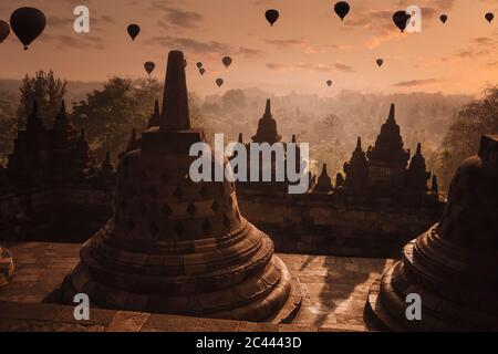 Indonesia, Giava Centrale, Magelang, Silhouette di mongolfiere che volano sopra il tempio di Borobudur al tramonto Foto Stock