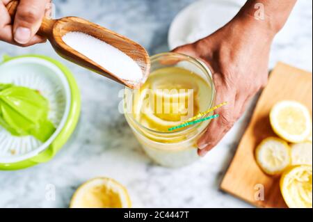 Mani di donna che aggiungono zucchero a caraffa di limonata fatta in casa Foto Stock