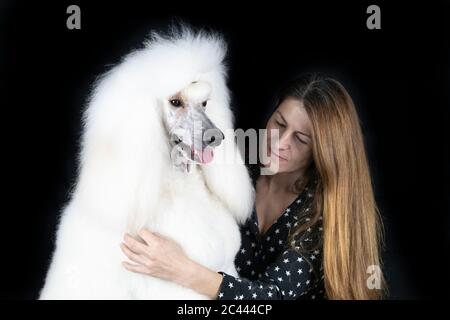 Ritratto di bianco Poodle standard e donna su sfondo nero Foto Stock