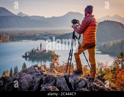 Slovenia, alta Carniola, Bled, uomo fotografando l'isola di Bled e Chiesa del pellegrinaggio di Assunzione di Maria all'alba foggy Foto Stock