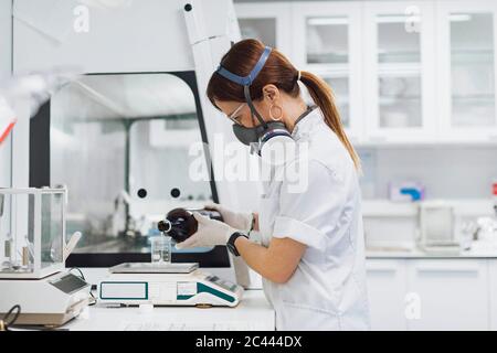 Medico che versa il prodotto chimico nel becher su bilancia mentre fa la ricerca in laboratorio Foto Stock