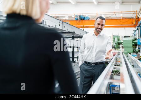 Uomo d'affari sorridente e donna a canne metalliche nella sala della fabbrica Foto Stock