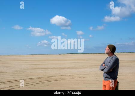 Riflessivo uomo maturo in piedi in spiaggia contro il cielo blu sulla giornata di sole Foto Stock