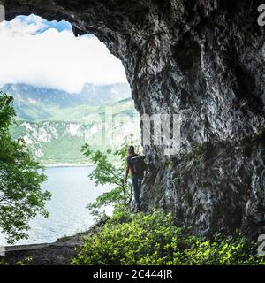 Escursionista maschile maturo in piedi da formazioni rocciose guardando il Lago di Como dall'ingresso della grotta Foto Stock