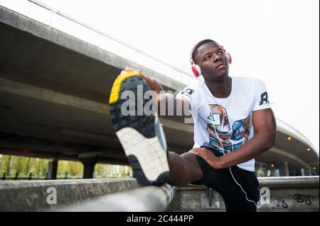 Giovane jogger che stretching la gamba e l'ascolto di musica in città Foto Stock