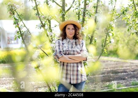 Ritratto di donna contadina matura sicura in piedi con le braccia incrociate al giardino comunitario Foto Stock