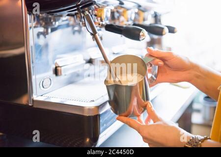 Mani di barista femminile che schiuma latte con macchina espresso in caffetteria Foto Stock