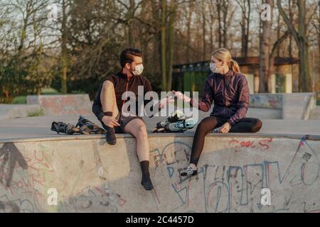 Donna che dà uomo mani igienizzatore mentre si siede al parco skateboard durante COVID-19 Foto Stock