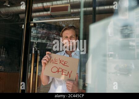 Negoziante in possesso di cartone con annuncio di apertura in città Foto Stock