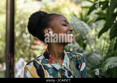 Felice giovane donna con gli occhi chiuso ascoltando musica con gli auricolari in giardino