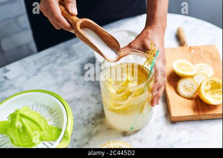 Mani di donna che aggiungono zucchero a caraffa di limonata fatta in casa Foto Stock