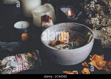 Primo piano di piante secche, erbe e petali di fiori di rosa gialla in una pentola di argilla grigia e sporca. Wiccan strega altare con ingredienti per la fusione incantesimo Foto Stock