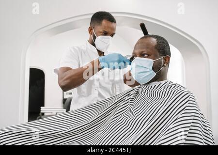 Barbiere indossare maschera chirurgica e guanti tagliando i capelli del cliente Foto Stock