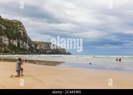 Nuova Zelanda, uomo che fotografa i leoni marini della Nuova Zelanda (Phocarctos hookeri) alla Baia di Purakaunui Foto Stock