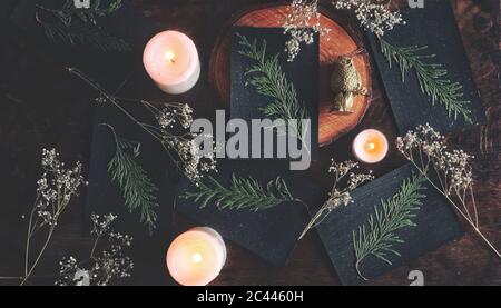 Piatto giacimento di carte Yule nero festivo fai da te (Natale) con ramo di cedro essiccato incollato su di esso. Decorazione naturale, candele brucianti Foto Stock