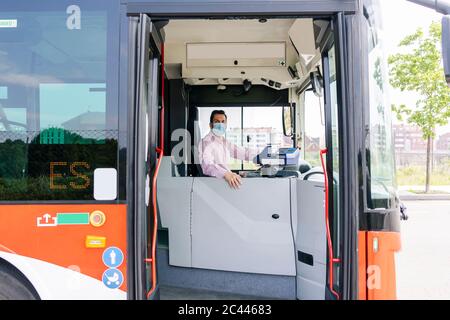 Autista maturo di autobus con maschera protettiva in attesa alla stazione degli autobus, Spagna Foto Stock