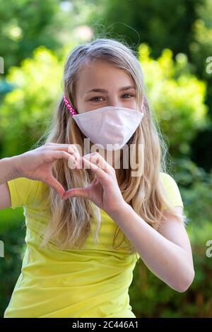 Primo piano di ragazza che indossa maschera faccia forma cuore con le mani nel parco Foto Stock
