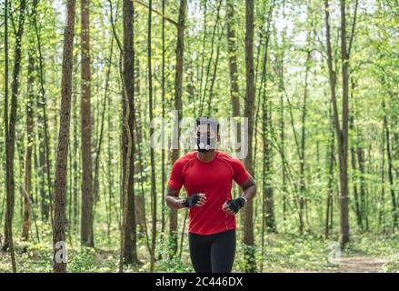 Sportivo che indossa maschera facciale che corre nella foresta Foto Stock