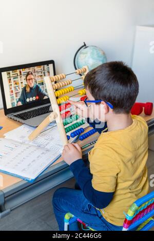 Studente elementare che usa abacus con insegnante in videochiamata durante la homeschooling Foto Stock