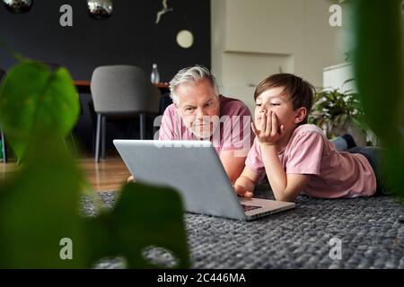 Padre e figlio si stendano sul pavimento, lavorando su un computer portatile Foto Stock